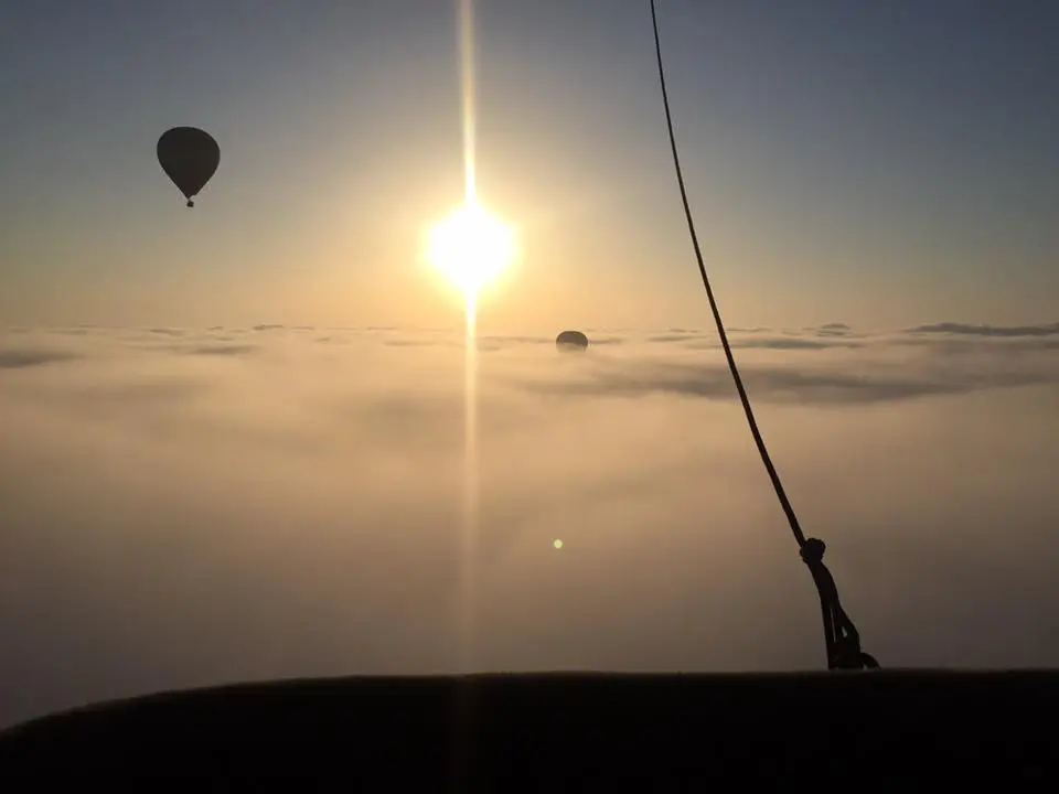 Several hot air balloons soar above the clouds in glorious sunshine